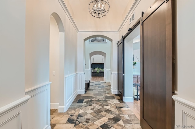 hall featuring visible vents, a chandelier, a barn door, arched walkways, and a decorative wall