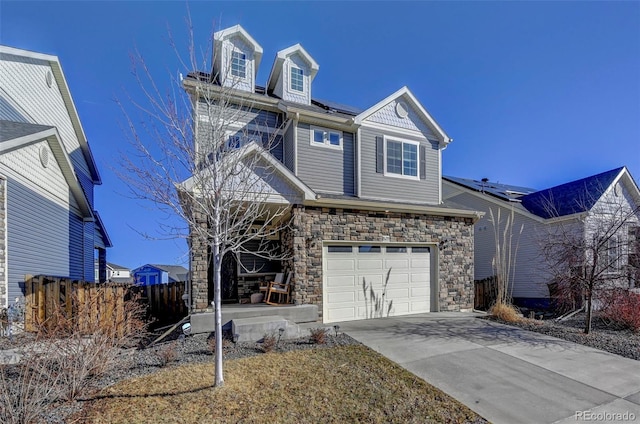 traditional home with driveway, stone siding, roof mounted solar panels, fence, and a garage