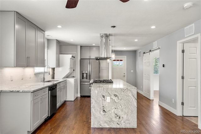 kitchen featuring a sink, a barn door, estacked washer and dryer, island exhaust hood, and appliances with stainless steel finishes
