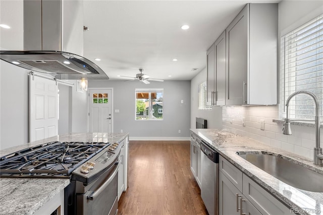 kitchen with a sink, stainless steel appliances, island range hood, baseboards, and decorative backsplash
