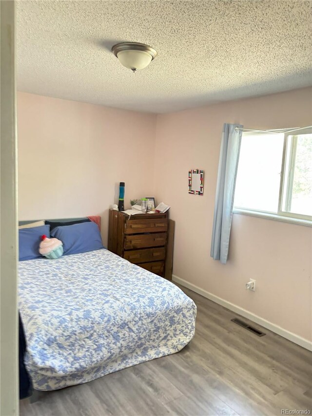 428 Prospect Ave, La Junta, CO 81050 - bedroom with visible vents, baseboards, a textured ceiling, and wood finished floors