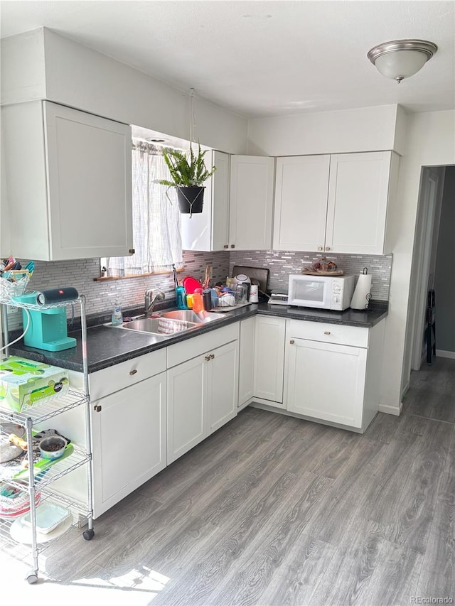 428 Prospect Ave, La Junta, CO 81050 - kitchen featuring dark countertops, decorative backsplash, white microwave, and light wood finished floors