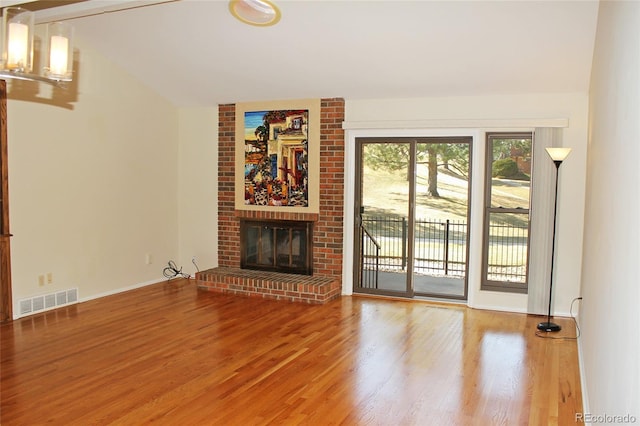 unfurnished living room featuring visible vents, lofted ceiling, wood finished floors, baseboards, and a brick fireplace