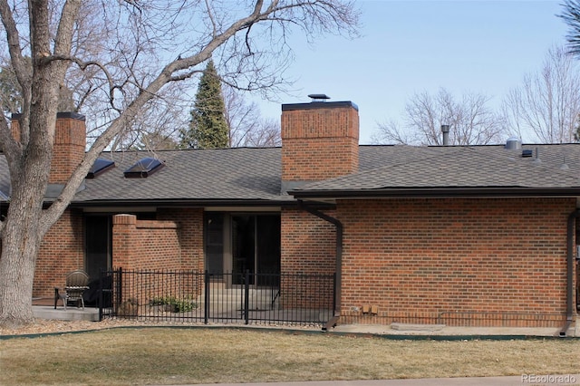 rear view of house with brick siding, roof with shingles, a chimney, and a patio area