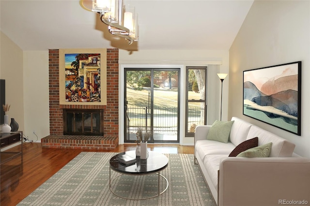 living room with vaulted ceiling, a brick fireplace, and wood finished floors