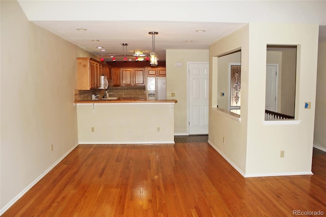 kitchen with pendant lighting, a peninsula, decorative backsplash, wood finished floors, and fridge with ice dispenser