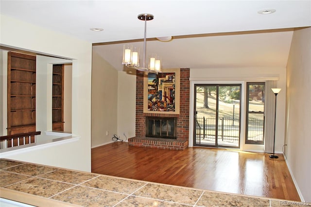 unfurnished living room with wood finished floors, baseboards, a brick fireplace, and a notable chandelier