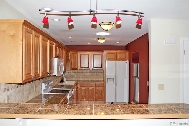kitchen featuring brown cabinets, tile counters, pendant lighting, white appliances, and tasteful backsplash