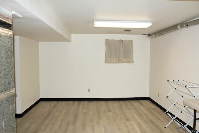 finished below grade area with baseboards, light wood finished floors, and visible vents