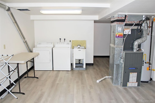 clothes washing area featuring heating unit, visible vents, washing machine and clothes dryer, laundry area, and light wood-type flooring