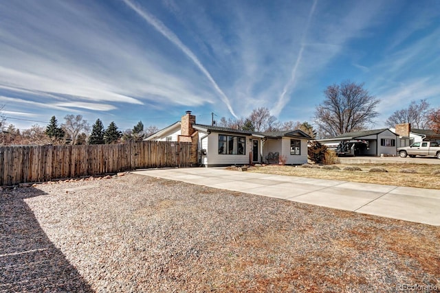 view of front facade with driveway, a chimney, and fence