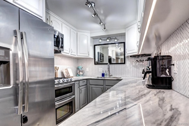 kitchen featuring gray cabinets, a sink, light stone counters, white cabinetry, and appliances with stainless steel finishes