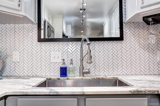 kitchen featuring decorative backsplash, stainless steel microwave, white cabinetry, and a sink