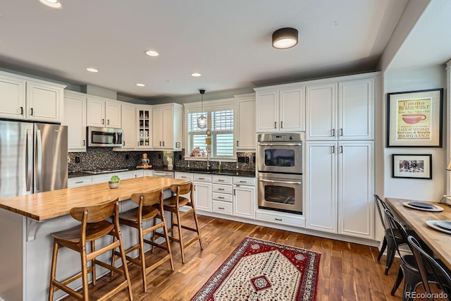 3386 Beeler Ct, Denver, CO 80238 - kitchen featuring appliances with stainless steel finishes, wood counters, wood finished floors, a breakfast bar area, and white cabinetry