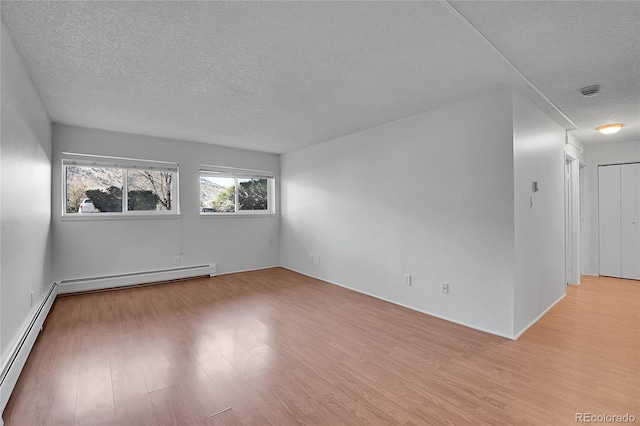 empty room with light wood finished floors, a baseboard heating unit, and a textured ceiling