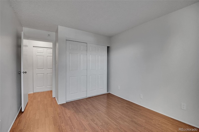 unfurnished bedroom featuring a textured ceiling, a closet, and light wood-style flooring