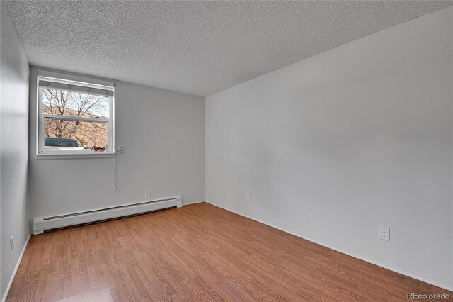 spare room featuring a textured ceiling, baseboard heating, and wood finished floors