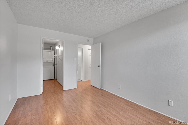 unfurnished bedroom featuring a walk in closet, a closet, a textured ceiling, stacked washing maching and dryer, and light wood-type flooring