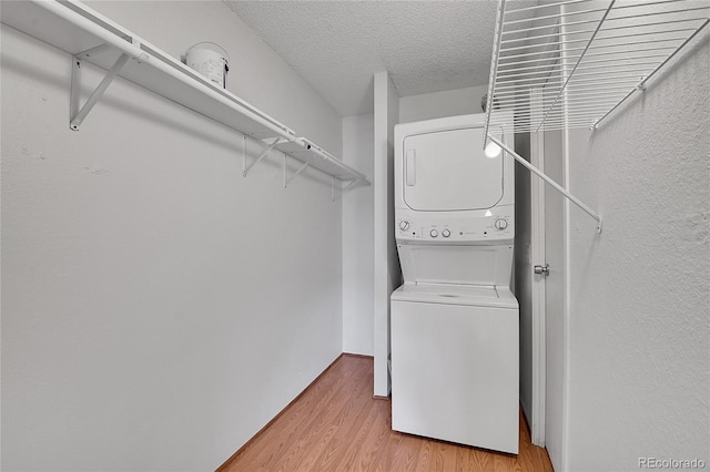 laundry room with a textured ceiling, laundry area, light wood-style floors, and stacked washer / drying machine