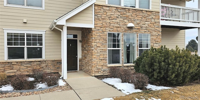 snow covered property entrance with stone siding