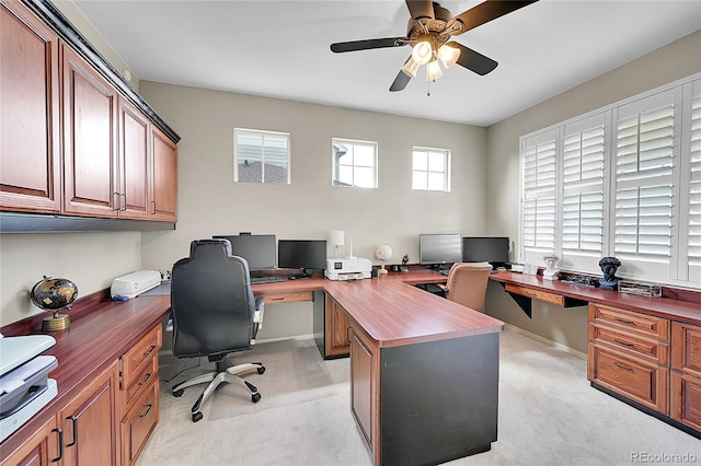 office space with baseboards, ceiling fan, built in desk, and light colored carpet