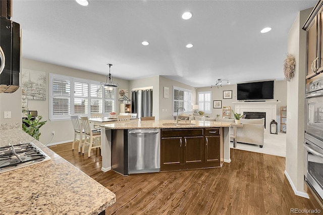 kitchen featuring dark brown cabinets, appliances with stainless steel finishes, a sink, a glass covered fireplace, and dark wood-type flooring