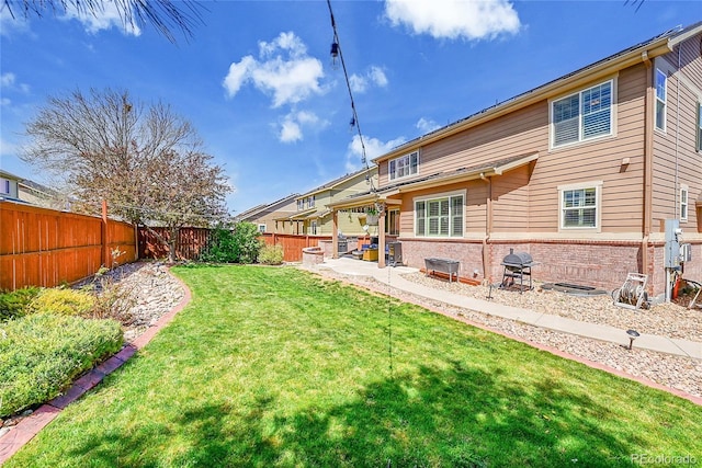 rear view of property with a lawn, brick siding, a fenced backyard, and a patio area