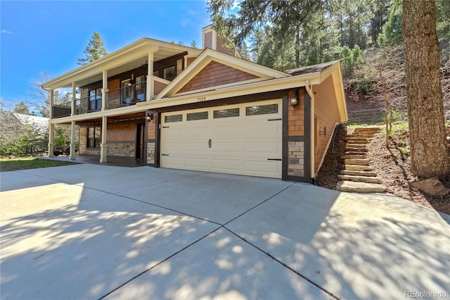 view of front of house featuring concrete driveway, stone siding, a balcony, and a chimney