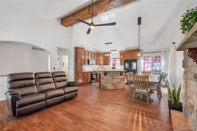 living area with high vaulted ceiling, a ceiling fan, beamed ceiling, wood finished floors, and arched walkways