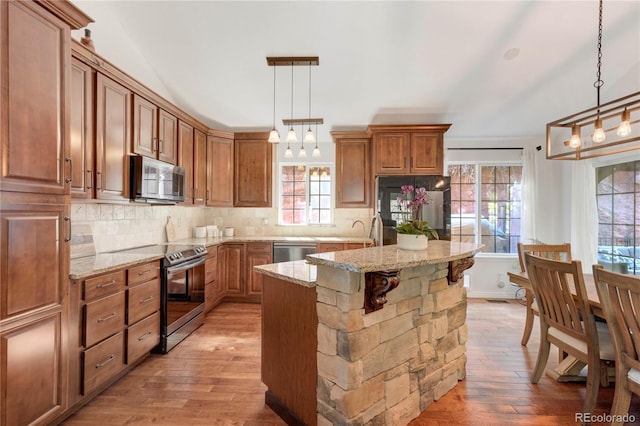 kitchen with stainless steel appliances, light wood-type flooring, brown cabinetry, a kitchen island, and a chandelier