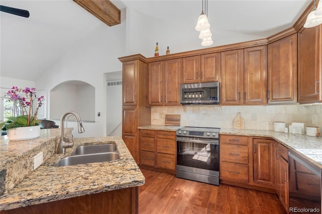 kitchen with stainless steel appliances, a sink, high vaulted ceiling, backsplash, and brown cabinetry