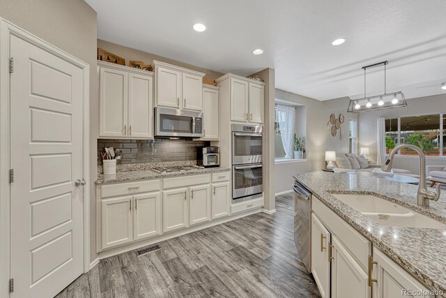 22583 E Union Cir, Aurora, CO 80015 - kitchen featuring appliances with stainless steel finishes, open floor plan, light wood finished floors, white cabinets, and tasteful backsplash
