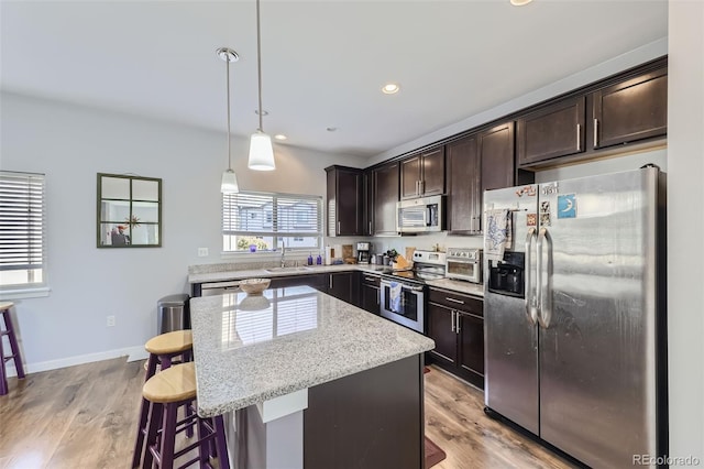 kitchen with appliances with stainless steel finishes, a center island, a kitchen breakfast bar, decorative light fixtures, and light hardwood / wood-style flooring