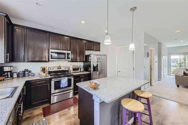 kitchen featuring a kitchen island, appliances with stainless steel finishes, light hardwood / wood-style floors, dark brown cabinetry, and decorative light fixtures