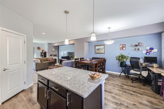 kitchen featuring dark brown cabinets, light stone counters, light hardwood / wood-style floors, decorative light fixtures, and a center island