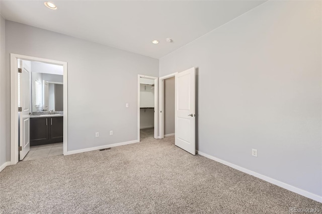 unfurnished bedroom featuring light carpet, a walk in closet, a closet, and ensuite bath