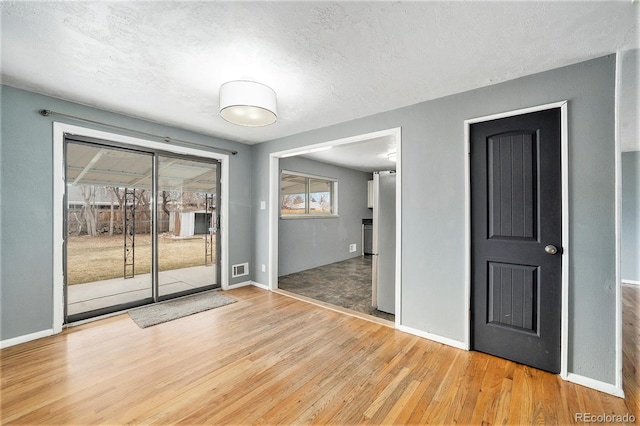 spare room with baseboards, light wood-style floors, and a textured ceiling