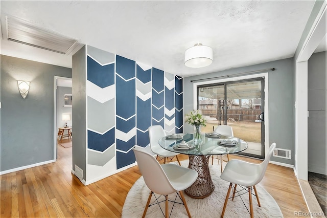 dining room featuring visible vents, baseboards, wood finished floors, and an accent wall