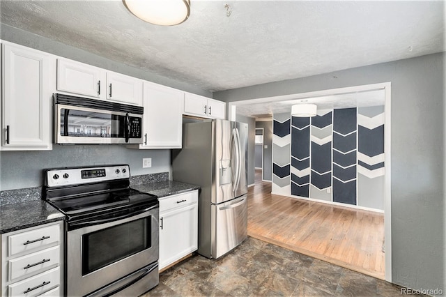 kitchen with stone finish floor, stainless steel appliances, dark stone counters, white cabinets, and baseboards