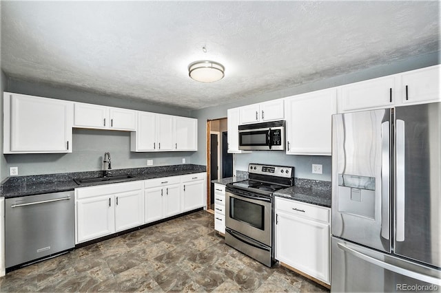 kitchen with stone finish floor, appliances with stainless steel finishes, white cabinets, a textured ceiling, and a sink