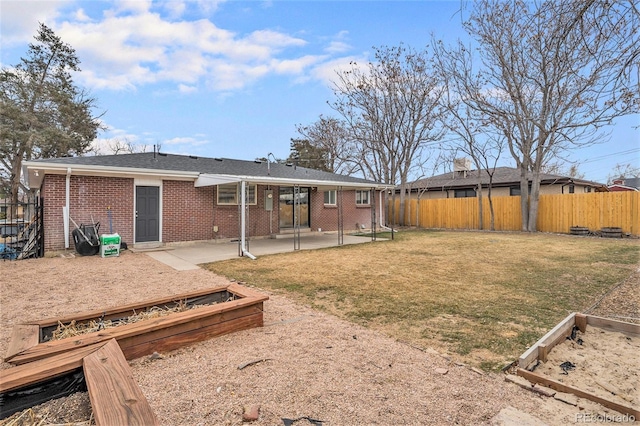 back of house with a garden, a fenced backyard, a lawn, a patio area, and brick siding