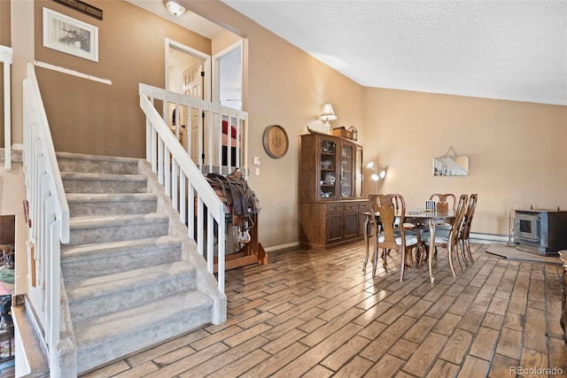 dining space with stairway, lofted ceiling, baseboards, a wood stove, and baseboard heating