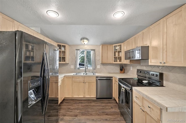 kitchen with stainless steel appliances, a sink, light brown cabinetry, a textured ceiling, and tile countertops