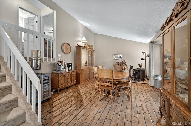 dining room featuring vaulted ceiling, stairway, a textured ceiling, light wood-style floors, and wine cooler
