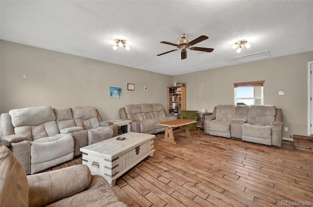 living room with ceiling fan, a textured ceiling, wood finished floors, and attic access