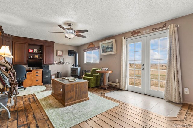home office featuring french doors, a ceiling fan, a wood stove, a textured ceiling, and baseboard heating
