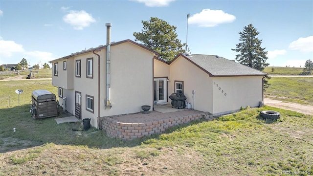 back of house with stucco siding, a lawn, and a patio area