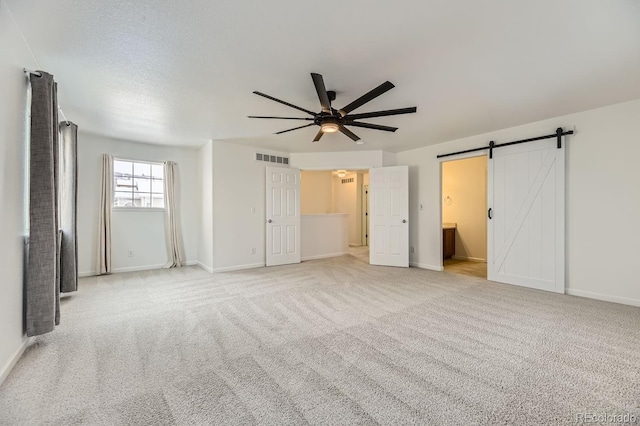 unfurnished bedroom with connected bathroom, ceiling fan, light carpet, and a barn door