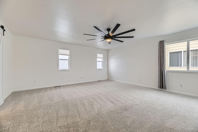 spare room featuring carpet, ceiling fan, a barn door, and a textured ceiling