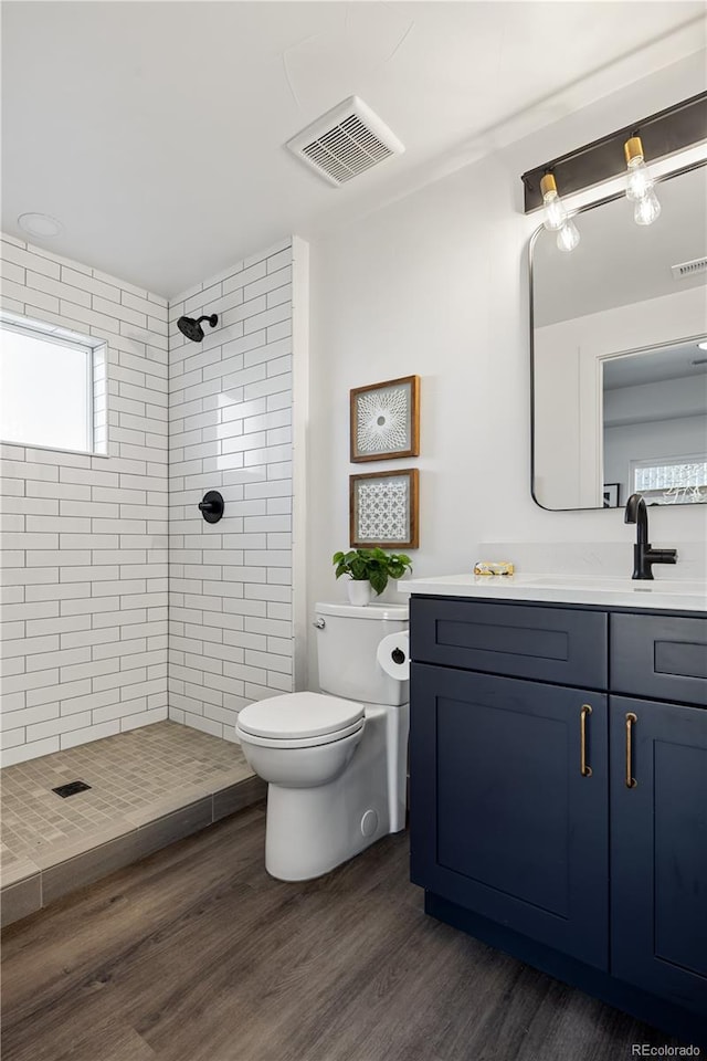 full bath with toilet, tiled shower, vanity, and visible vents